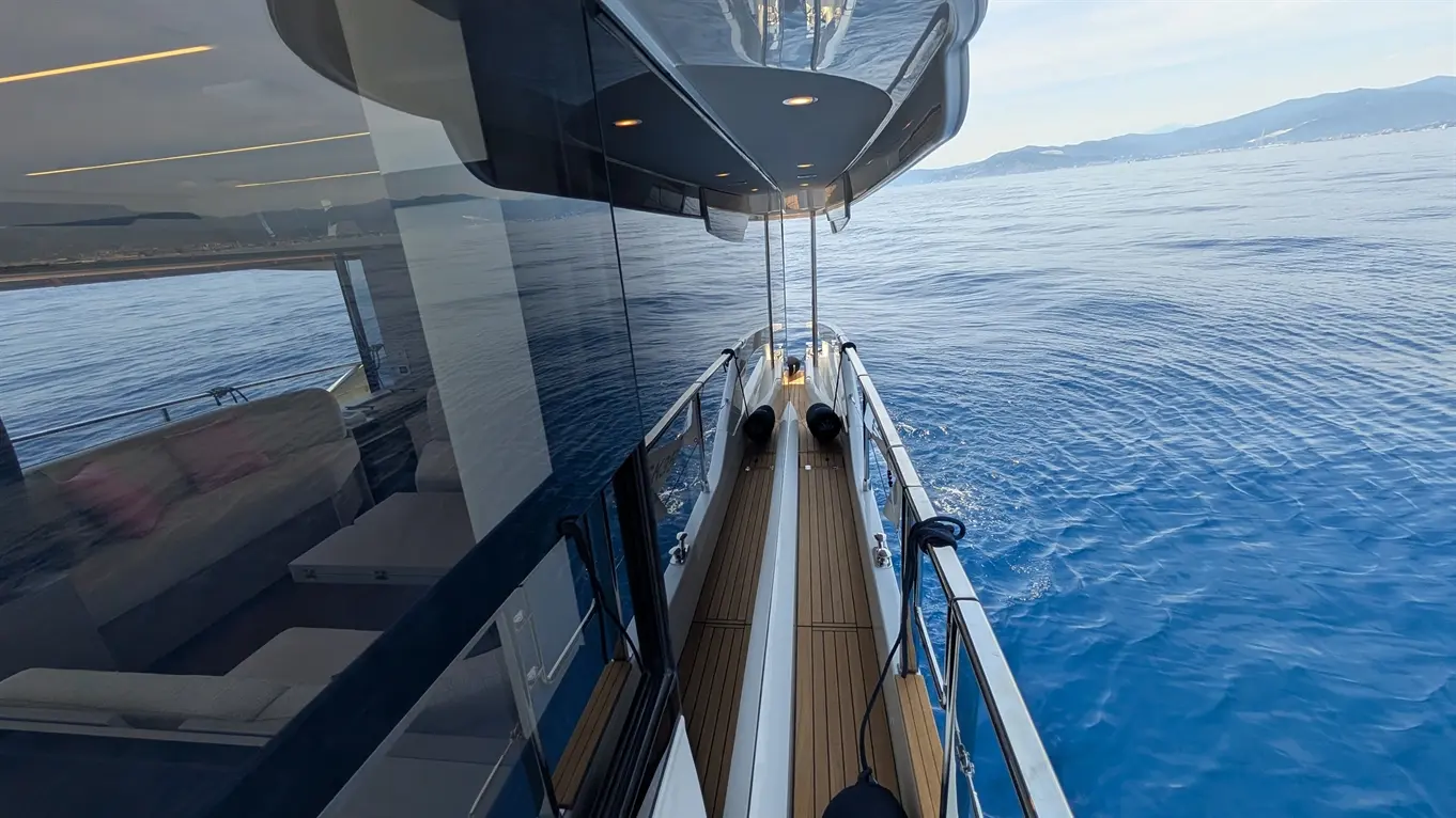 View from a luxury yacht's deck showing sleek lines, polished surfaces, and calm blue waters, reflecting distant coastline.